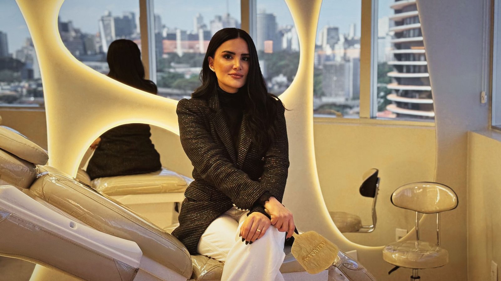 Dra. Lais Bueno na sala de atendimento iluminada, com vista para Belo Horizonte